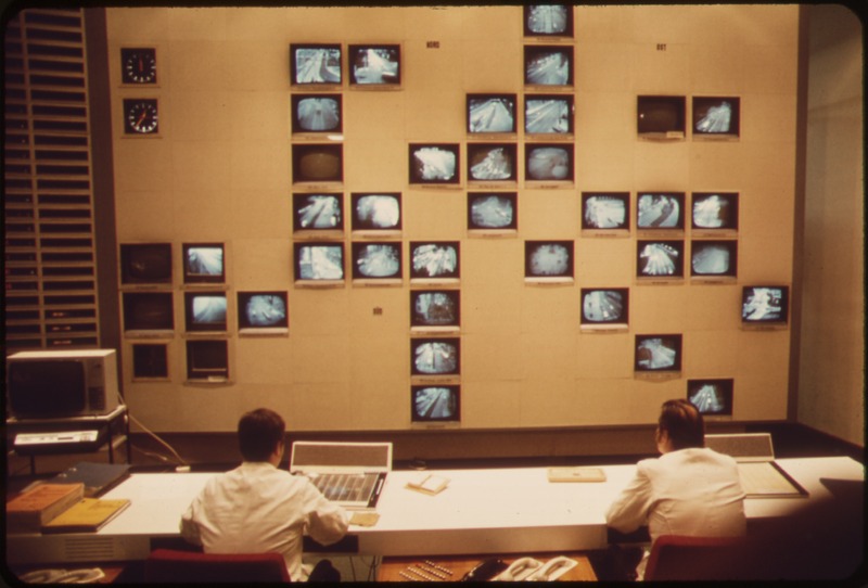 Monitoring CCTV w Centralnym Posterunku Policji w Monachium, Niemcy, 1973 r. Dwie osoby przy biurku patrzące na monitory na ścianie